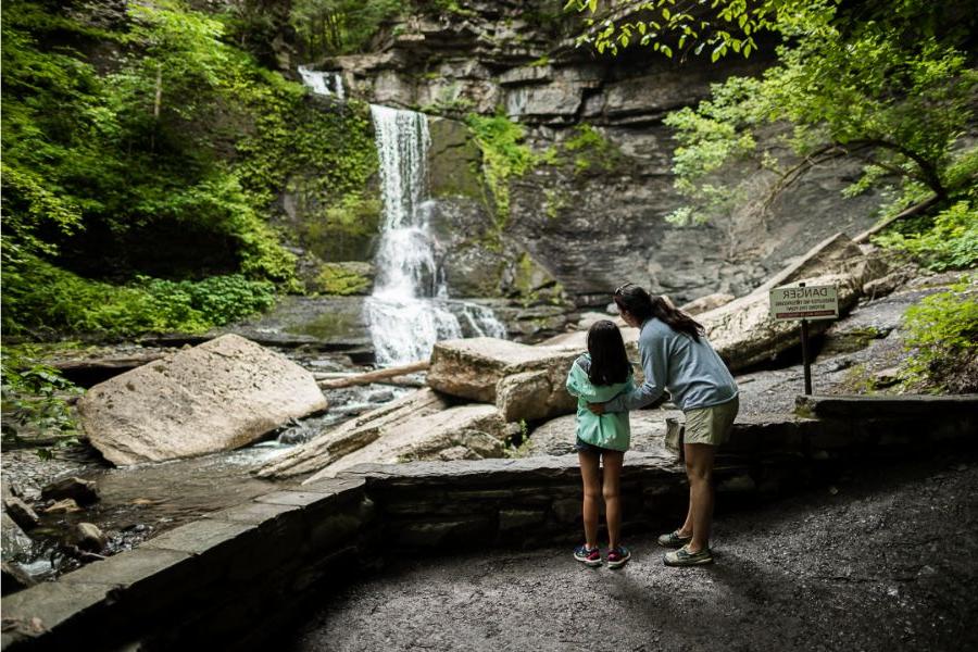 A mother and young daughter looking at a waterfall in the fall at Fillmore Glen State Park